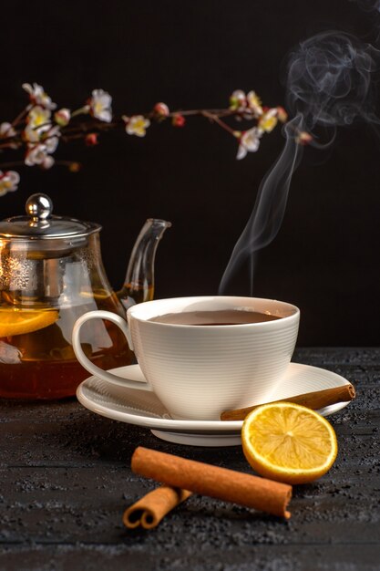 Vista frontale tazza di tè con limone cannella e bollitore sulla superficie grigia