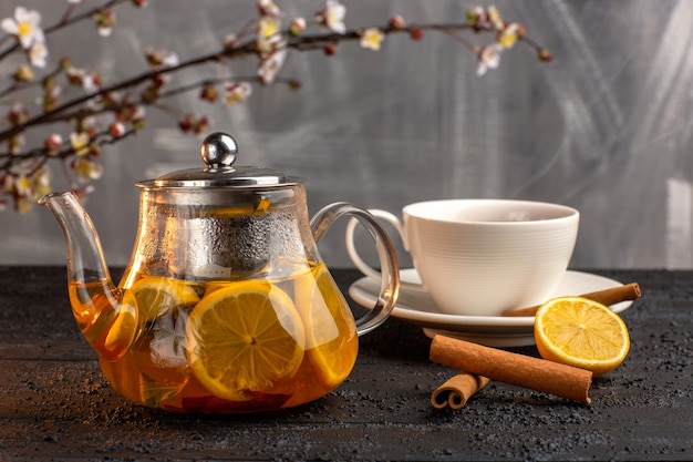 Vista frontale tazza di tè con limone cannella e bollitore sulla superficie grigia