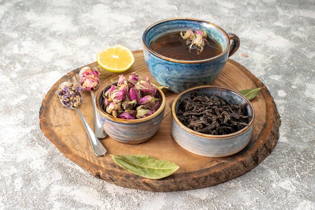 Vista frontale tazza di tè con limone e fiori su sfondo chiaro cerimonia della colazione sapore frutta colore cibo fiori mattutini
