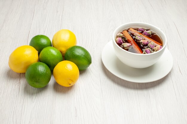 Vista frontale tazza di tè con limoni freschi sul colore bianco degli agrumi della frutta del tè dello scrittorio