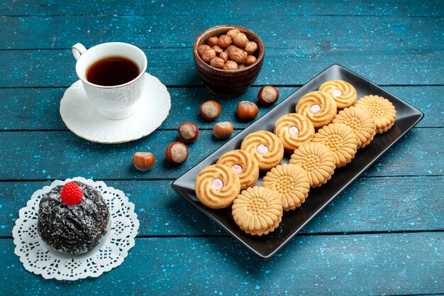 Vista frontale tazza di tè con noci e biscotti sulla torta di biscotto dolce del biscotto dello zucchero dello scrittorio blu rustico