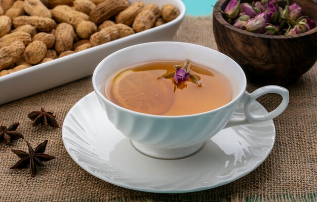 Vista frontale tazza di tè con una fetta di limone e arachidi con fiori secchi