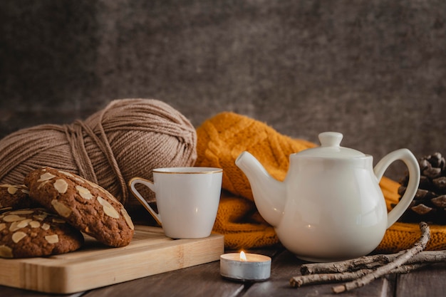 Vista frontale tazza e teiera con biscotti e filato