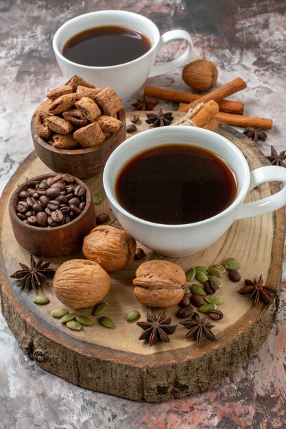 Vista frontale tazze di caffè con cannella e noci su zucchero chiaro biscotto color tè cacao dolce