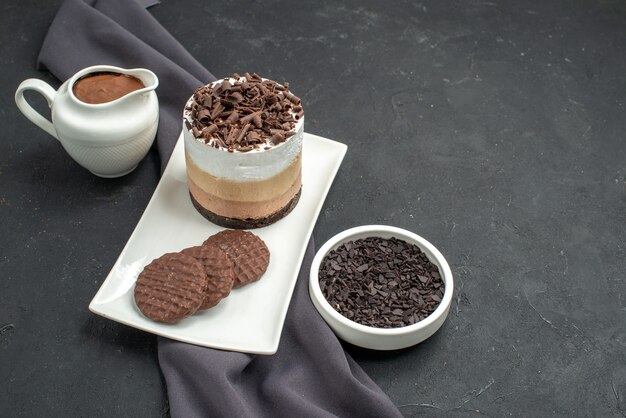 Vista frontale torta al cioccolato e biscotti su ciotole di piatto rettangolare bianco con scialle viola al cioccolato su sfondo scuro isolato spazio libero