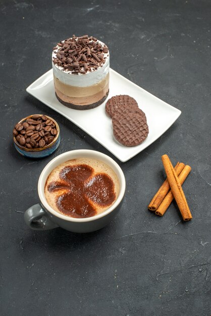 Vista frontale torta al cioccolato e biscotti su piatto rettangolare bianco tazza di caffè bastoncini di cannella ciotola