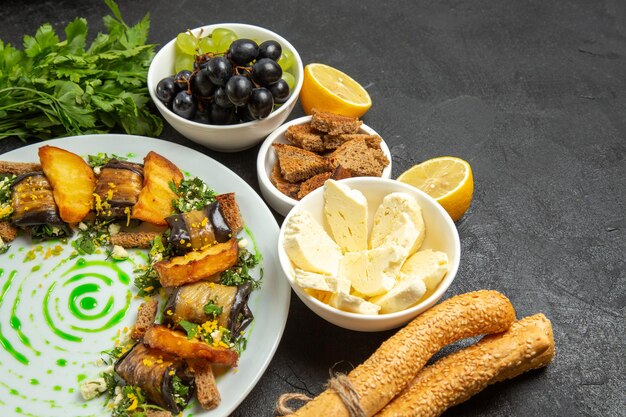 Vista frontale uva fresca e morbida con verdure al formaggio bianco e involtini di melanzane su sfondo scuro pasto alimentare frutti di latte