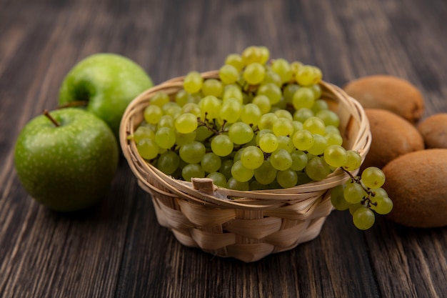 Vista frontale uva verde in un cesto con mele verdi e kiwi su uno sfondo di legno