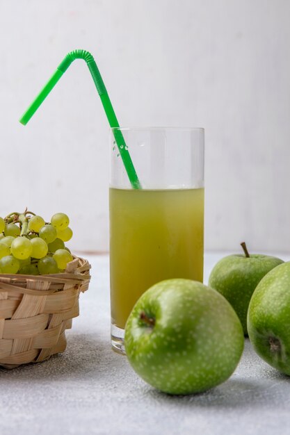 Vista frontale uva verde in un cesto con pera mele verdi e succo di mela con una cannuccia verde in un bicchiere su uno sfondo bianco