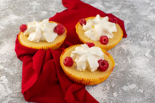 Vista frontale vicino torte con crema buonissimo progettato con lamponi sulla superficie grigia