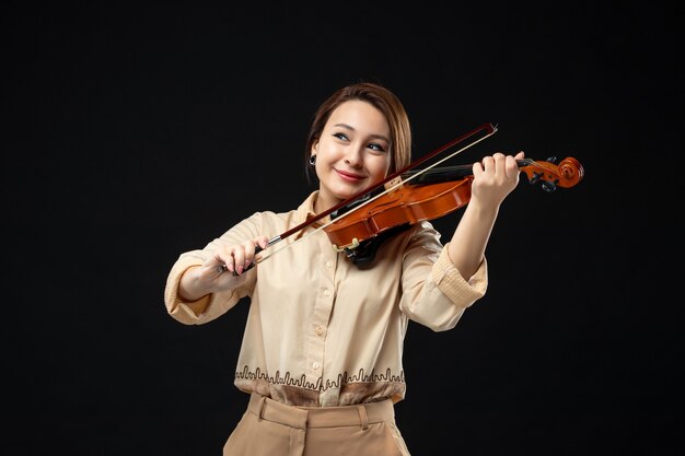 Vista frontale violinista femminile che suona il violino con il sorriso sul viso sullo strumento da concerto di musica da parete scura suona la melodia emozione donna