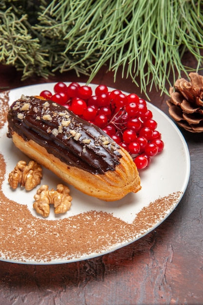 Vista frontale yummy choco eclairs con bacche rosse sul dolce da dessert torta torta piano scuro