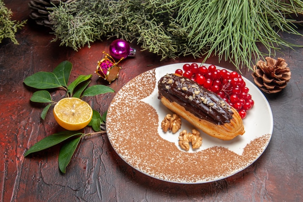 Vista frontale yummy choco eclairs con bacche rosse sul dolce da dessert torta torta tavolo scuro