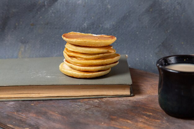 Vista frontale yummy deliziose frittelle con tazza nera di latte sulla prima colazione pasto cibo sfondo grigio