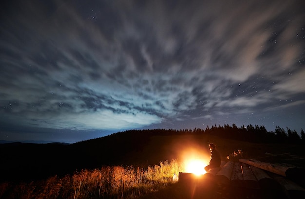 Vista grandangolare sulla notte stellata nuvolosa in montagna e un uomo che si gode la natura