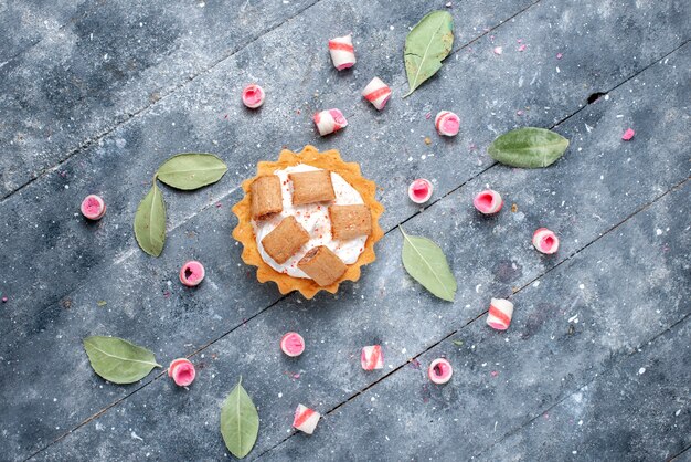 Vista in lontananza deliziosa torta cremosa con biscotti insieme a caramelle a fette su grigio