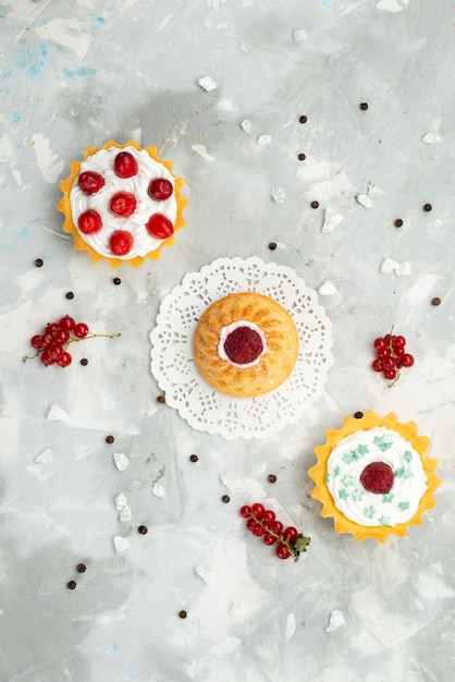 Vista in lontananza piccolo d torte con panna e diversi frutti isolati sulla superficie leggera zucchero dolce