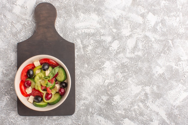 Vista in lontananza superiore insalata di verdure fresche con cetrioli affettati pomodori oliva e formaggio bianco all'interno della piastra sul pasto di insalata di cibo vegetale scrivania grigia