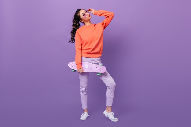 Vista integrale della ragazza coreana alla moda con lo skateboard. Studio shot di splendida donna asiatica holding longboard su sfondo viola.