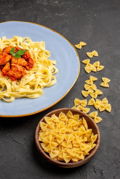 Vista laterale appetitosa ciotola di pasta accanto al piatto di una pasta appetitosa con sugo e carne sul tavolo scuro