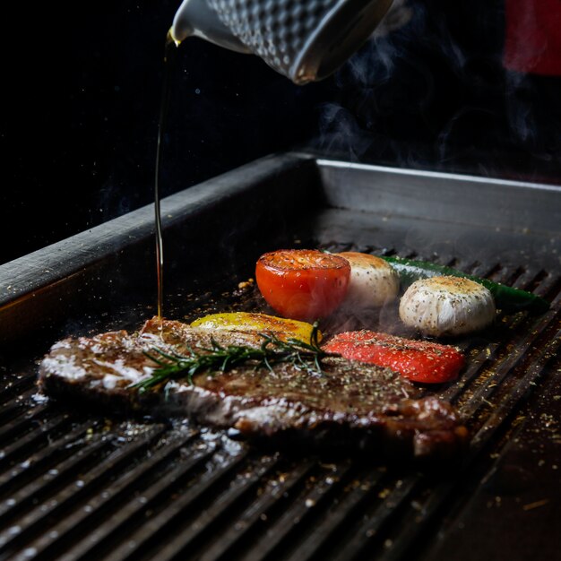 Vista laterale bistecca alla griglia con rosmarino e olio e funghi nel barbecue