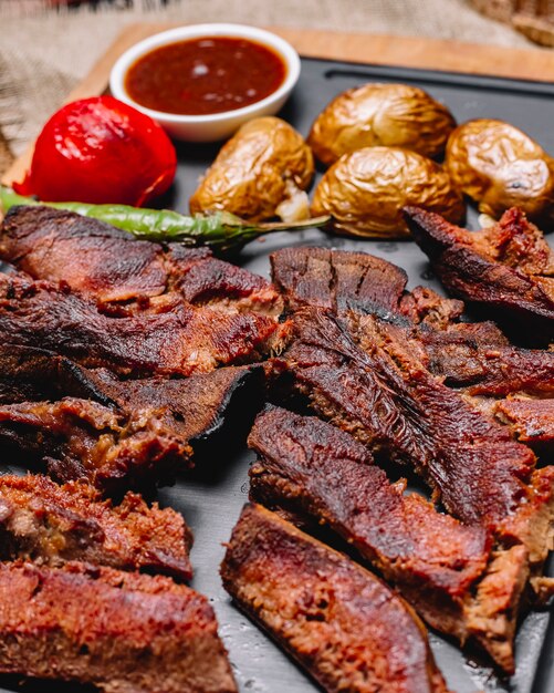 Vista laterale carne alla griglia con patate e verdure grigliate con salse