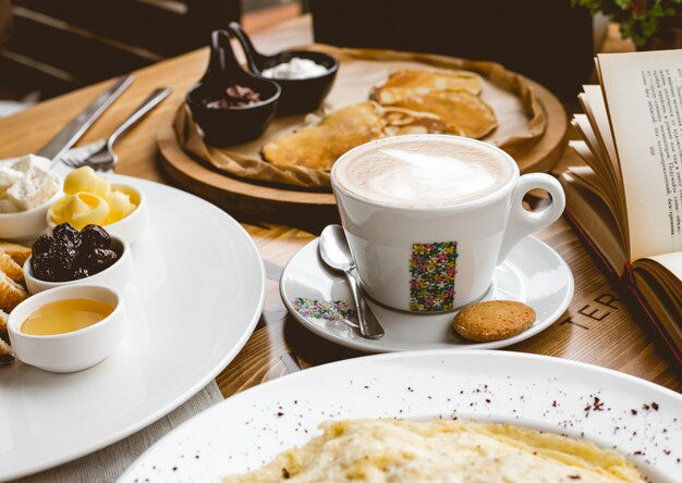 Vista laterale colazione tazza di cappuccino con antipasti e frittelle con marmellata