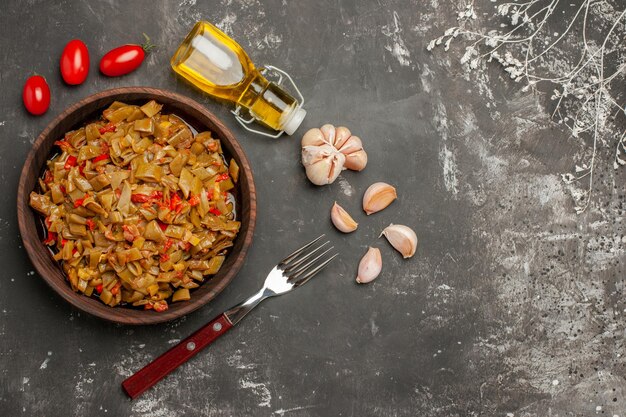 Vista laterale da lontano piatto appetitoso aglio bottiglia di olio pomodori forchetta e un piatto appetitoso accanto ai rami degli alberi sul tavolo scuro