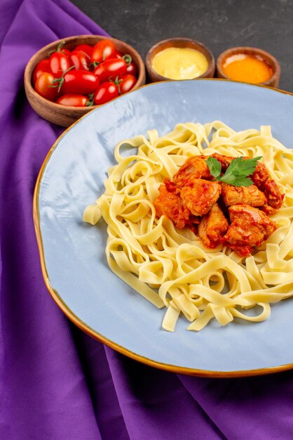 Vista laterale da lontano piatto di pasta e salse con pasta e sugo di carne tra ciotole di pomodori e due tipi di salse sulla tovaglia viola