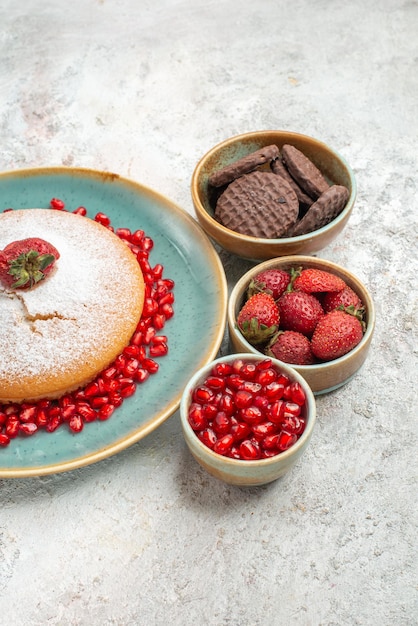 Vista laterale da lontano torta un'appetitosa torta alla fragola ciotole di biscotti al melograno e frutti di bosco