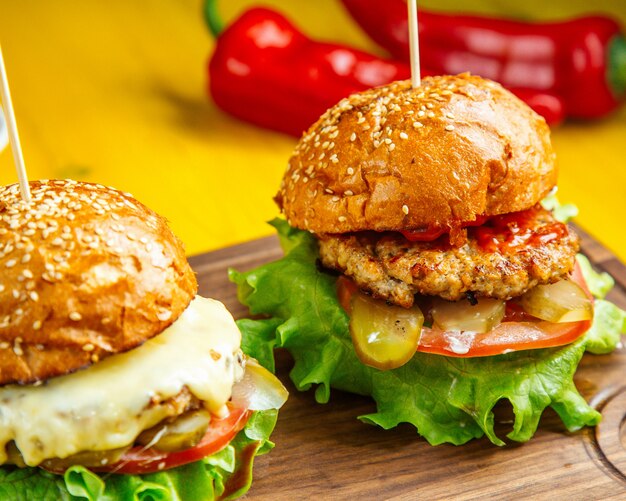 Vista laterale degli hamburger con i pomodori e i sottaceti del formaggio fusi cotoletta del pollo sul bordo di legno