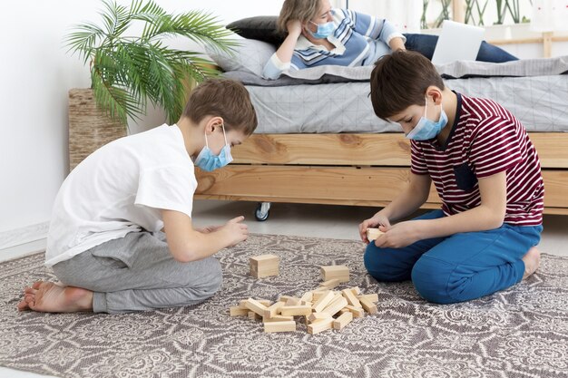 Vista laterale dei bambini con le maschere mediche che giocano jenga a casa