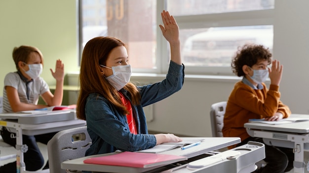 Vista laterale dei bambini con maschere mediche che imparano a scuola