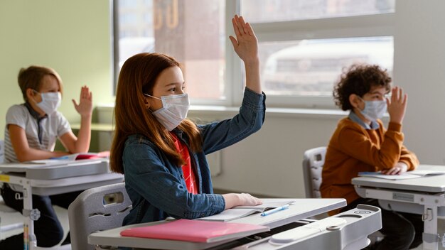 Vista laterale dei bambini con maschere mediche che imparano a scuola