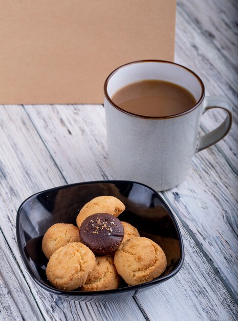 Vista laterale dei biscotti in una ciotola nera e in una tazza con cacao su di legno