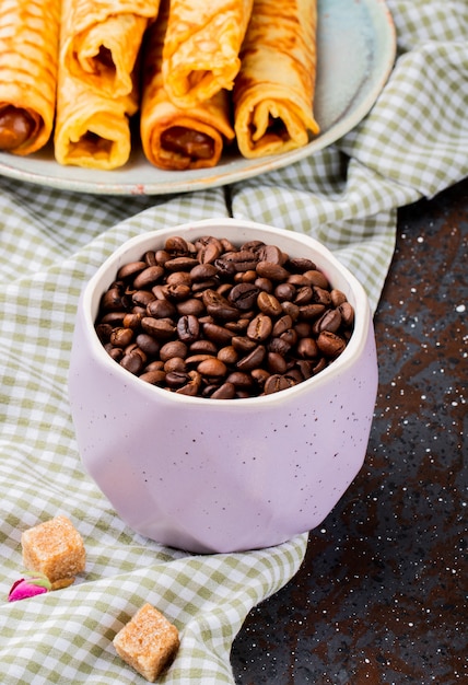 Vista laterale dei chicchi di caffè arrostiti in una ciotola e nei rotoli del wafer con latte condensato su un piatto