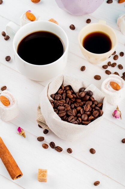 Vista laterale dei chicchi di caffè in un sacco e tazze di caffè su fondo bianco