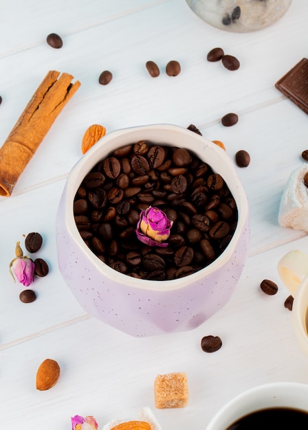 Vista laterale dei chicchi di caffè in una ciotola e bastoni di cannella su fondo bianco