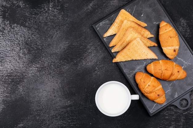 Vista laterale dei croissant con i toast e lo spazio della copia e del latte sull'orizzontale nero del fondo