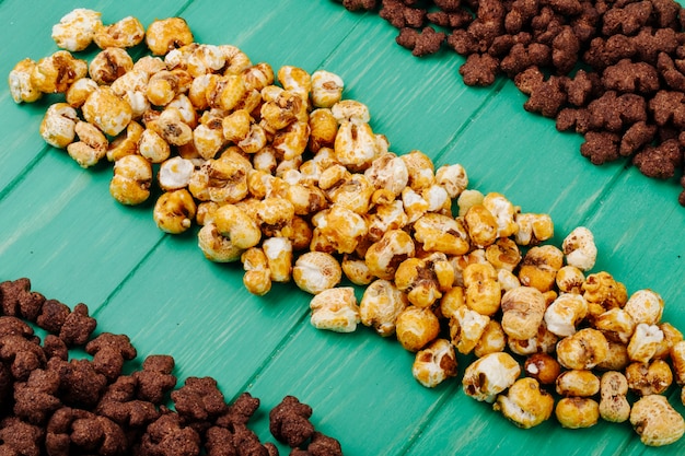 Vista laterale dei fiocchi di mais croccanti del cioccolato e dei popcorn del caramello su fondo di legno verde