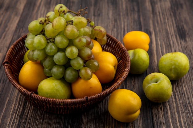 Vista laterale dei frutti come uva verde pluot e nectacots nel cesto e modello di pluots e nectacots su sfondo di legno