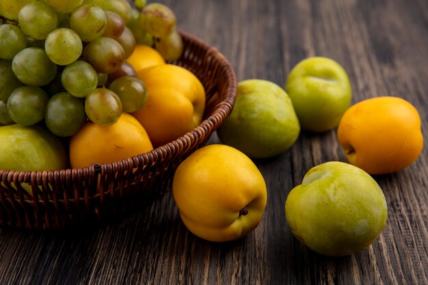 Vista laterale dei frutti come uva verde pluot e nectacots nel cesto e modello di pluots e nectacots su sfondo di legno