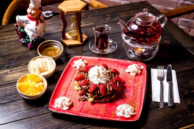 Vista laterale dei frutti e della teiera della crema del cioccolato alla panna della fragola del pancake