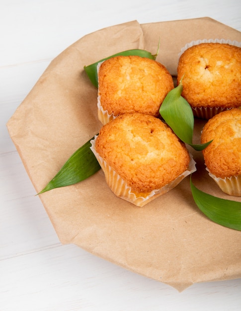 Vista laterale dei muffin con le foglie verdi sulla carta marrone del mestiere su legno rustico bianco