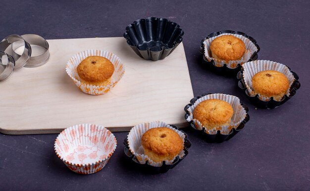 Vista laterale dei muffin in stampi di carta su un tagliere di legno e formine per biscotti su rustico