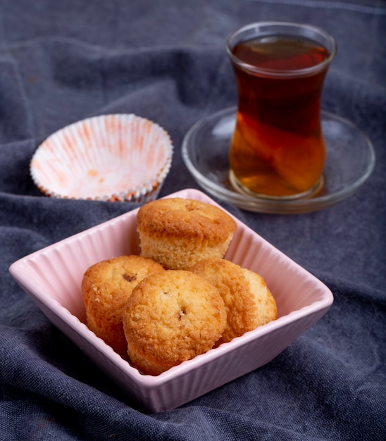 Vista laterale dei muffin in stampi di una ciotola di carta e vetro di armudu di tè su gray