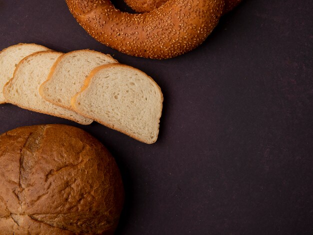 Vista laterale dei pani come fette classiche e bagel del pane bianco della pannocchia su fondo marrone rossiccio con lo spazio della copia