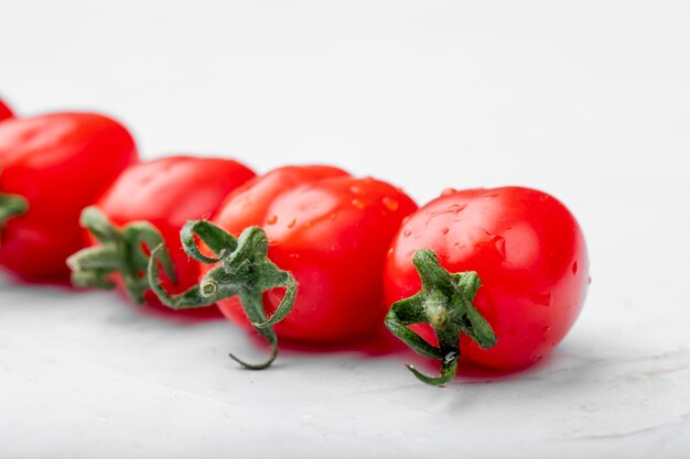 Vista laterale dei pomodori ciliegia freschi maturi con le gocce di acqua su fondo bianco