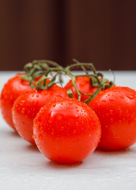 Vista laterale dei pomodori freschi bagnati su una superficie bianca