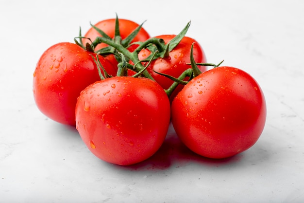 Vista laterale dei pomodori freschi maturi con le gocce dell'acqua su fondo bianco